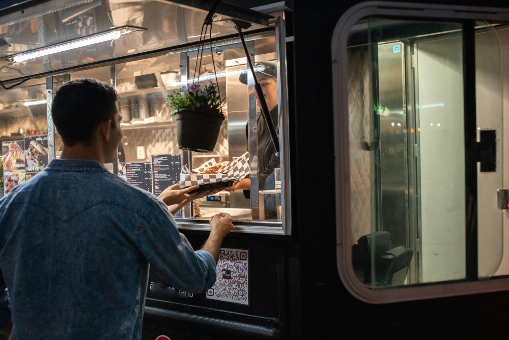 A food truck worker handing a hot, freshly prepared meal to a customer with a smile.