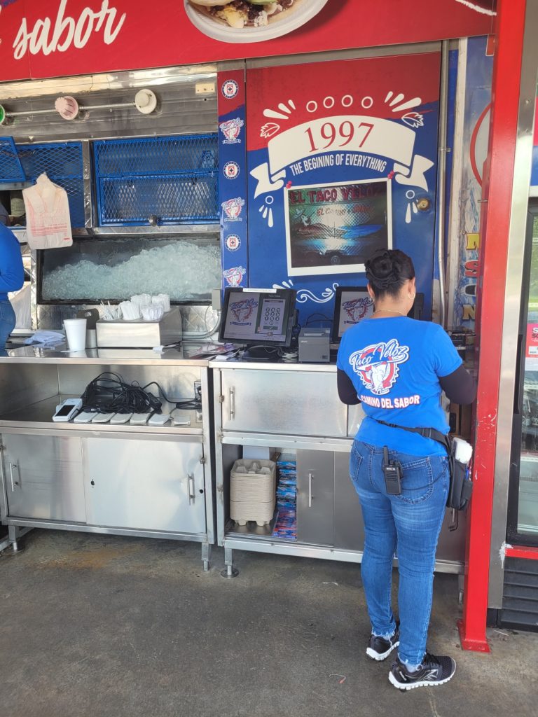 A bustling Taco Veloz food truck serving customers in a drive-up, Sonic-style layout.